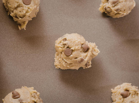 Several scoops of no-bake chocolate chip protein dough placed on brown parchment paper ready to be chilled.
